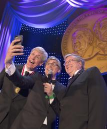 National Inventors Hall of Fame Induction Ceremony emcee Mo Rocca takes a selfie onstage with inductees Eric Fossum and Steve Sasson